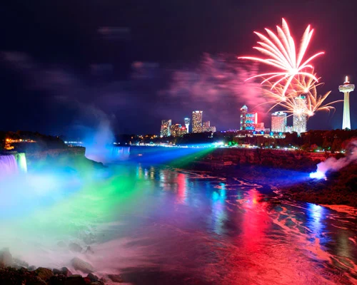 Waterval van Niagara Falls verlicht in groen, blauw en rood met vuurwerk boven de skyline van Niagara Falls bij nacht
