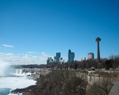 Besneeuwde oevers bij de Niagara Falls met opstijgende nevel en de Skylon Tower en skyline van Niagara Falls op de achtergrond