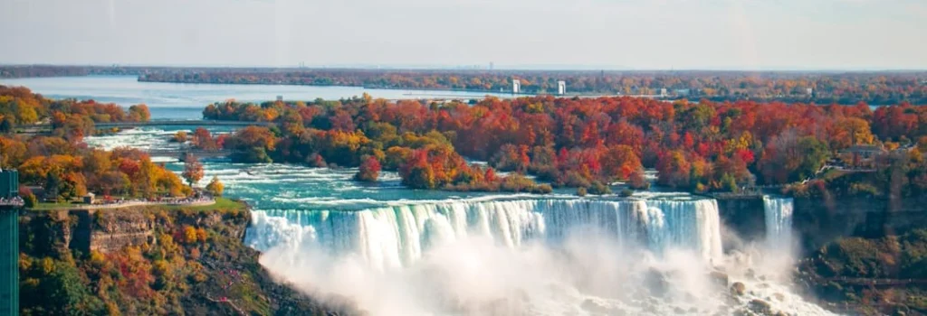 Luchtfoto van de brede Niagara watervallen omringd door bomen in herfsttinten met een rivier die uitmondt in een meer