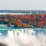 Luchtfoto van de brede Niagara watervallen omringd door bomen in herfsttinten met een rivier die uitmondt in een meer