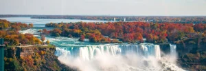 Luchtfoto van de brede Niagara watervallen omringd door bomen in herfsttinten met een rivier die uitmondt in een meer