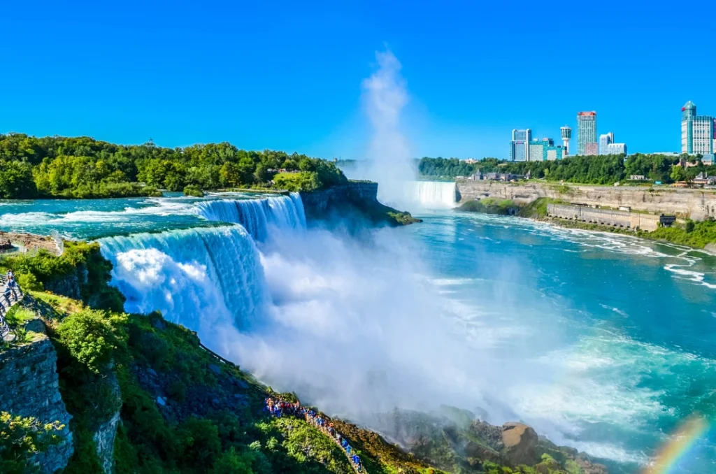 Panoramisch uitzicht op de bruisende Niagara watervallen met opstijgende waternevel en de skyline van de stad op de achtergrond