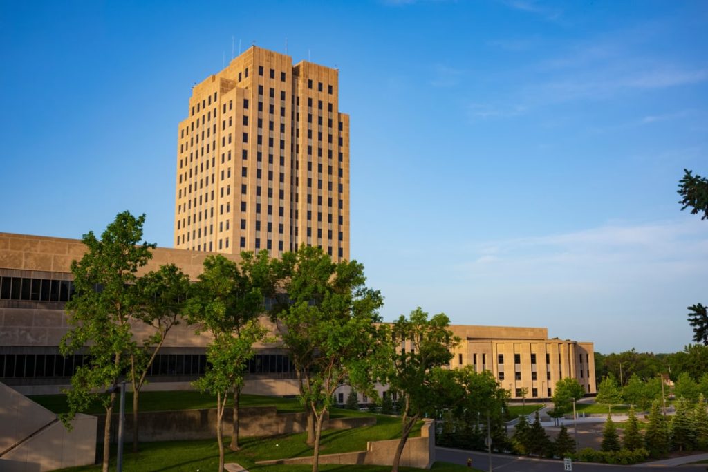 Hoge art-decotoren van het North Dakota State Capitol in Bismarck gezien tussen groene bomen bij zonsondergang
