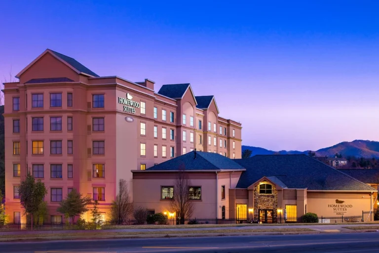 Buitenaanzicht van hotel Homewood Suites in North Carolina met verlichte gevel tegen een paarsblauwe avondlucht en bergen op de achtergrond
