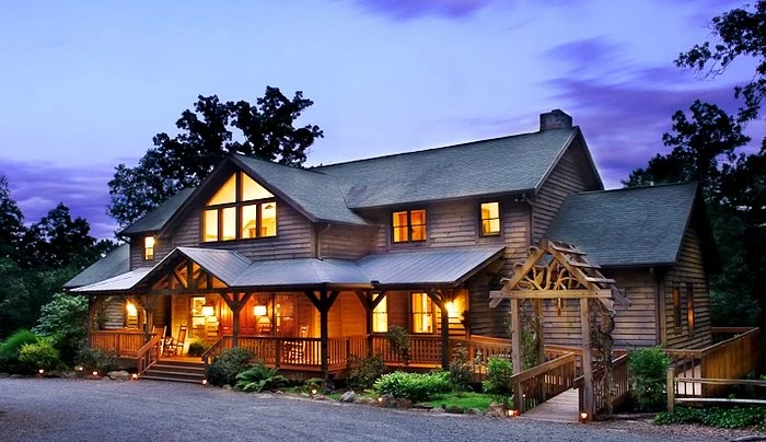 Een houten lodge met veranda en verlichte ramen staat te midden van bomen in North Carolina tijdens de schemering