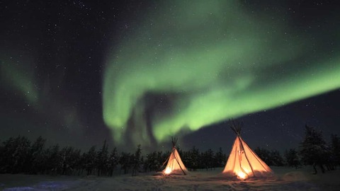 Twee van binnenuit verlichte tipi tenten in de sneeuw onder een helder groen noorderlicht en sterrenhemel
