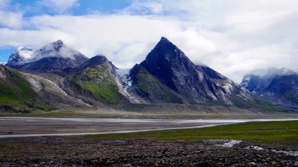 Rij ruige besneeuwde bergtoppen met een groene vallei op de voorgrond in Auyuittuq National Park in Nunavut