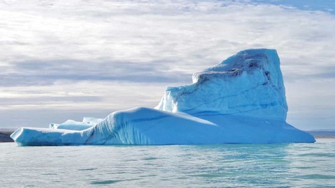 Grote witte ijsberg met scherpe randen drijft in kalm water onder een bewolkte hemel bij Pond Inlet in Nunavut