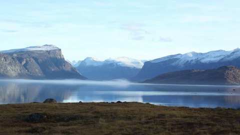 Laaghangende mist boven het kalme water van de Pangnirtung Fjord tussen besneeuwde bergtoppen in Nunavut