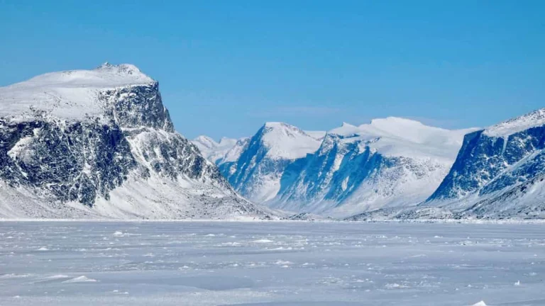 Steile rotswand met een dun laagje sneeuw aan de rand van de Pangnirtung Fjord in Nunavut boven kalm blauw water