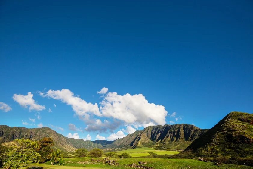 Weidse groene vallei op Oahu met een gekartelde bergketen onder een helderblauwe lucht met witte wolken