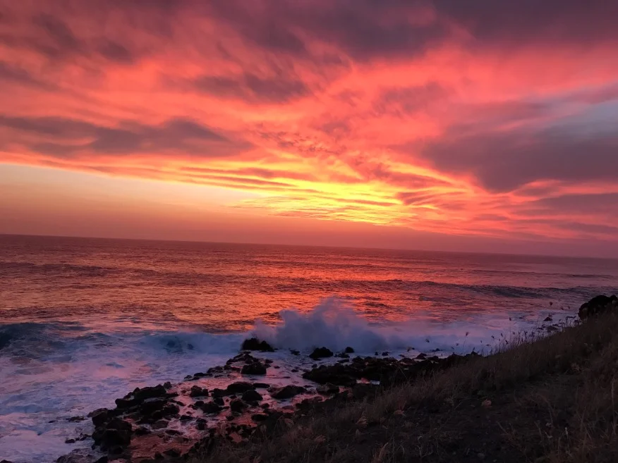 Felrode avondlucht boven de oceaan met brekende golven tegen rotsen bij Kaena Point op Oahu