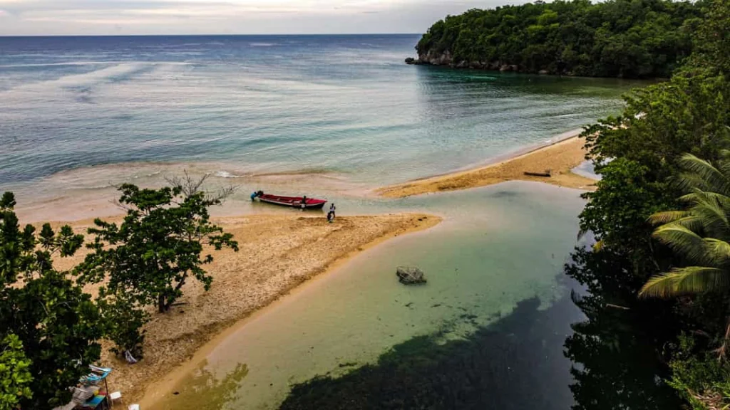 Luchtfoto van een klein zandstrand met een rode vissersboot in een rustige kreek tussen groene begroeiing bij Ocho Rios