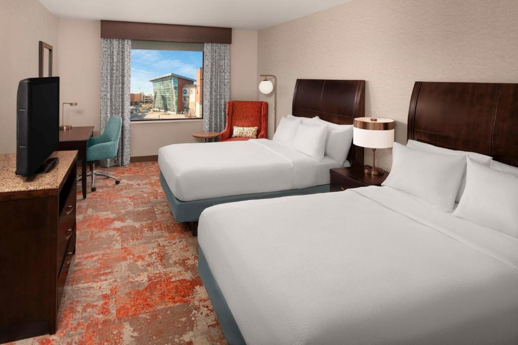 Hotelkamer met twee opgemaakte bedden, een televisie op een ladekast en een raam met stadszicht