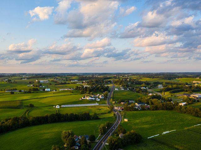 Luchtfoto van een kronkelende weg tussen groene velden, boerderijen en verspreide huizen in het Ohio platteland bij zonsondergang