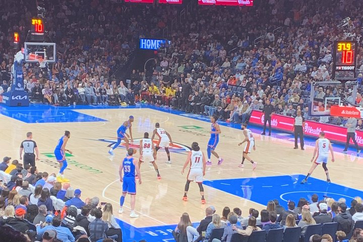 Basketbalwedstrijd in volle arena gezien vanaf de tribune, met spelers op het veld en schermen met de stand