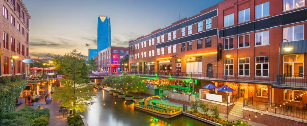 Verlicht kanaal in de wijk Bricktown met bakstenen pakhuizen, terrassen en een rondvaartboot bij avondlicht