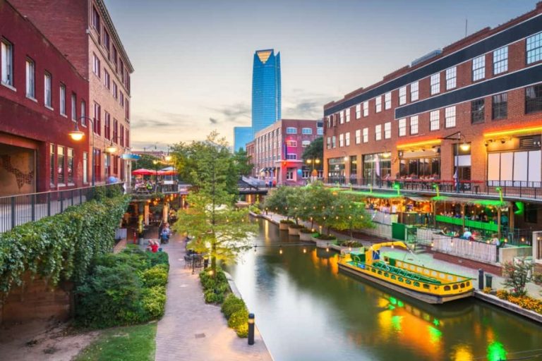 Een geel rondvaartbootje ligt afgemeerd bij het verlichte Bricktown kanaal in Oklahoma City tijdens de schemering