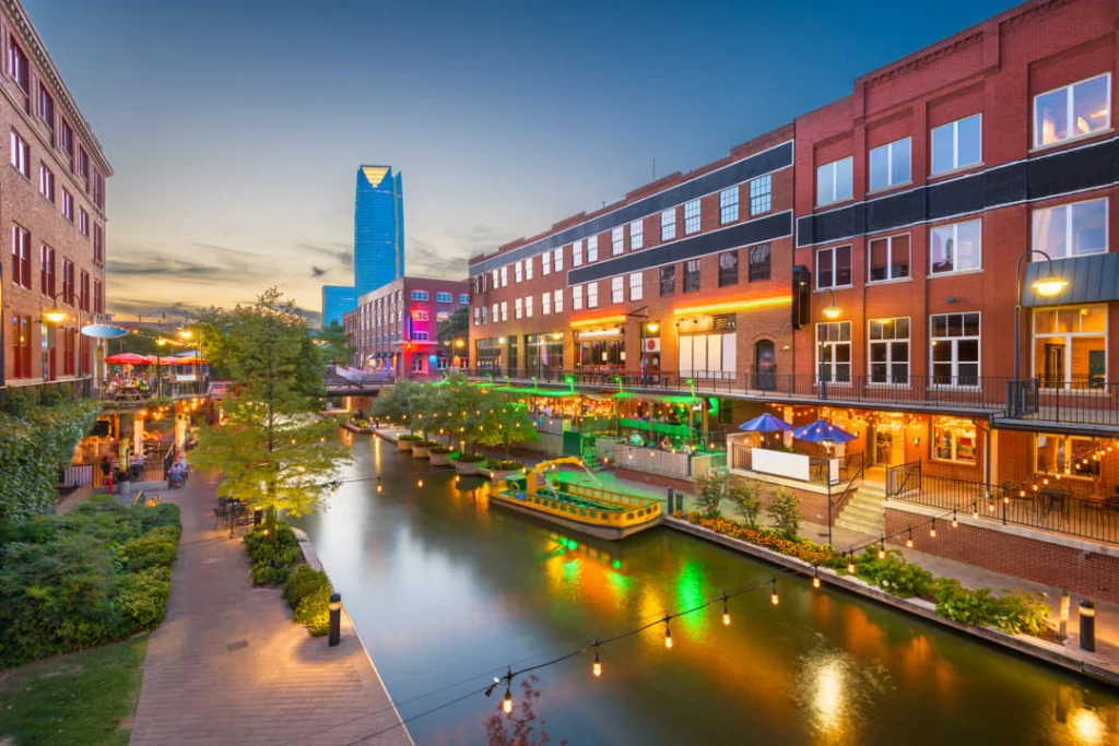 Kanaal in de wijk Bricktown met verlichte terrassen en bakstenen gebouwen, met een glazen wolkenkrabber op de achtergrond
