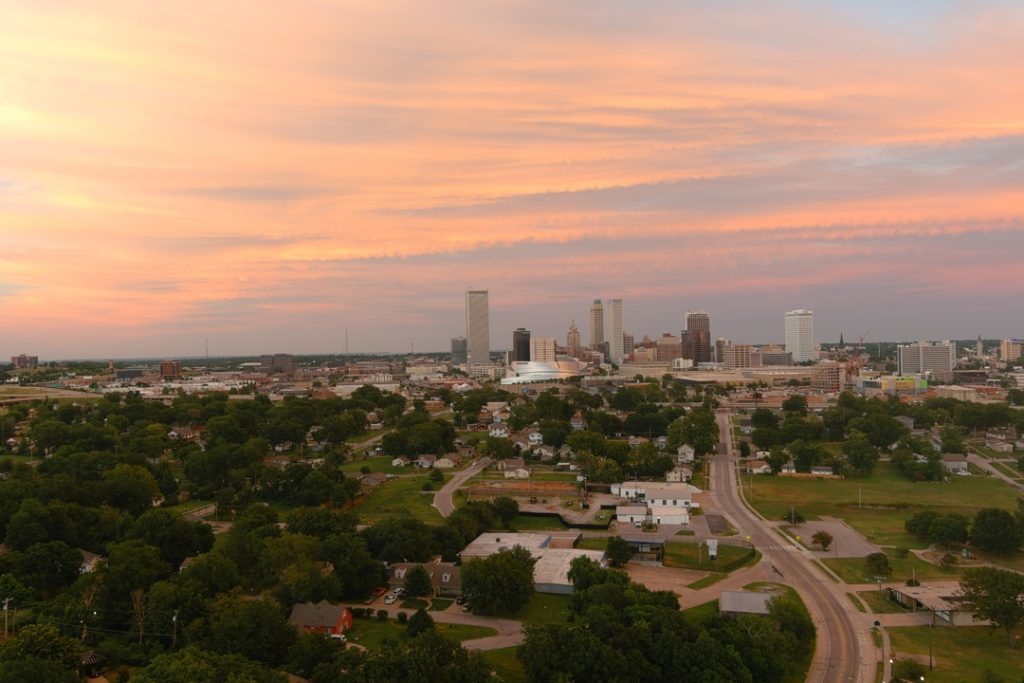Uitgestrekte luchtfoto van woonwijken met op de achtergrond de wolkenkrabbers van Oklahoma City onder een roze en oranje avondlucht