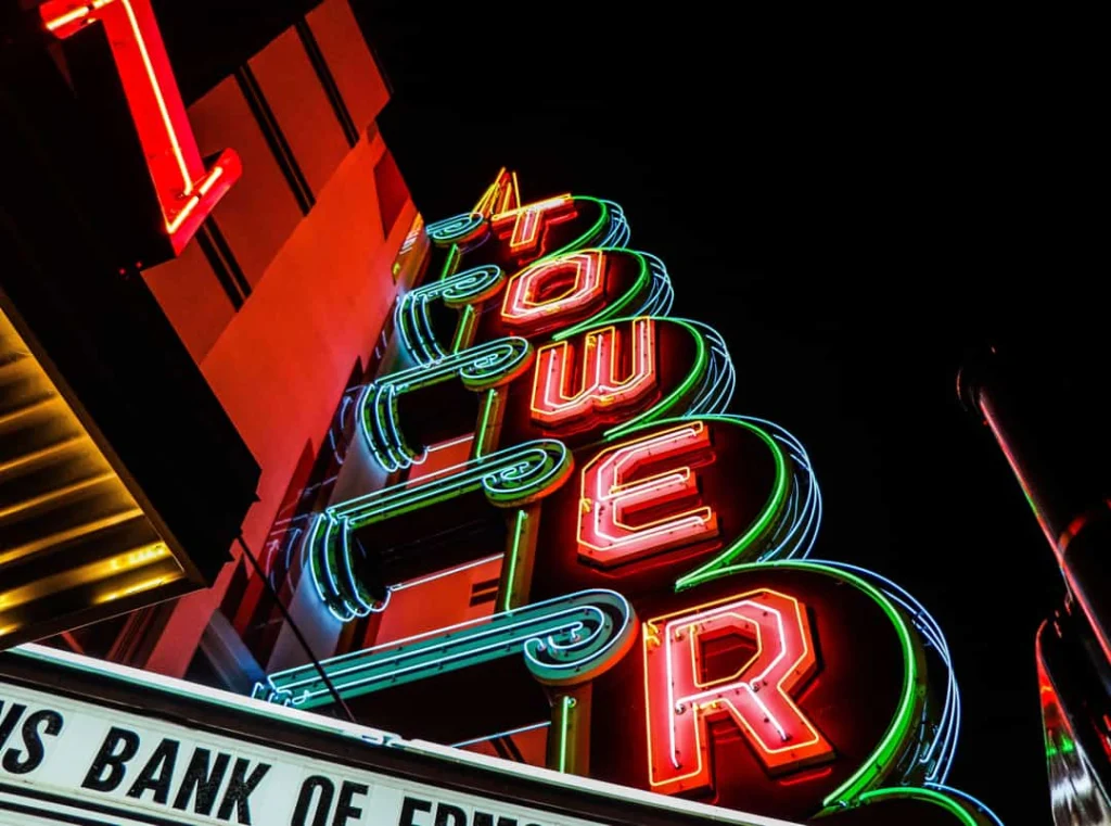 Fel oplichtend neonuithangbord met de tekst tower tegen een donkere avondlucht boven een theatergevel