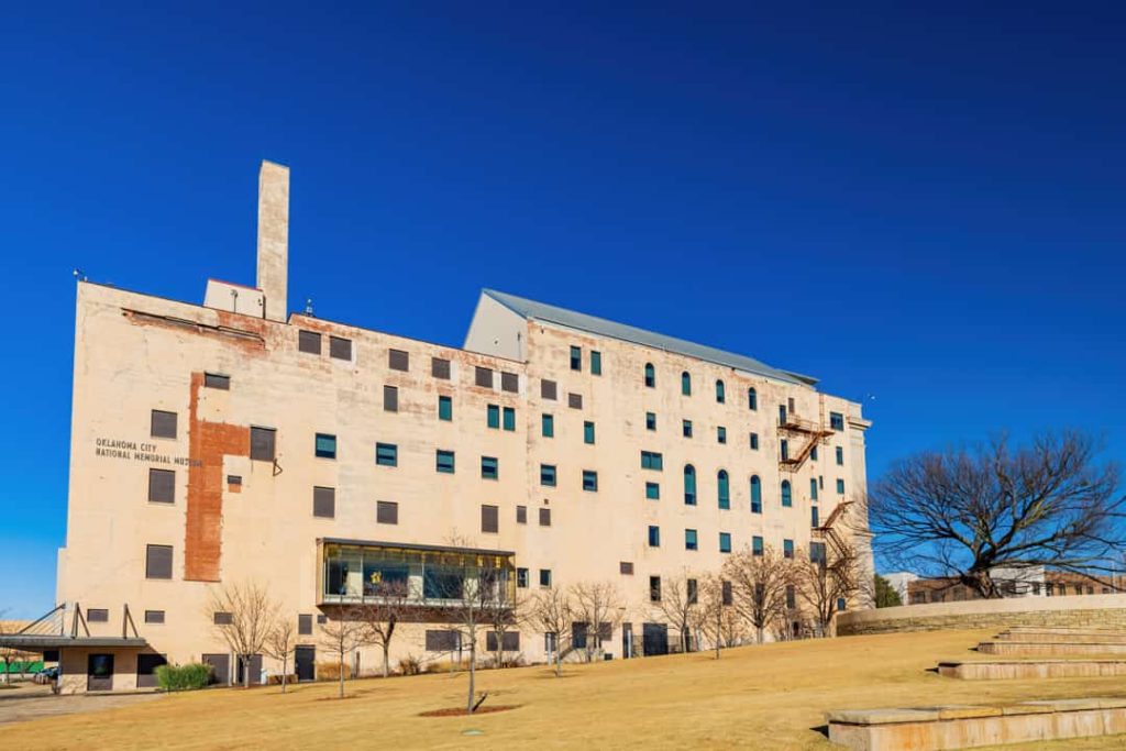 Beschadigd wit gebouw met veel ramen, onderdeel van het Oklahoma City National Memorial Museum, tegen een strakblauwe lucht