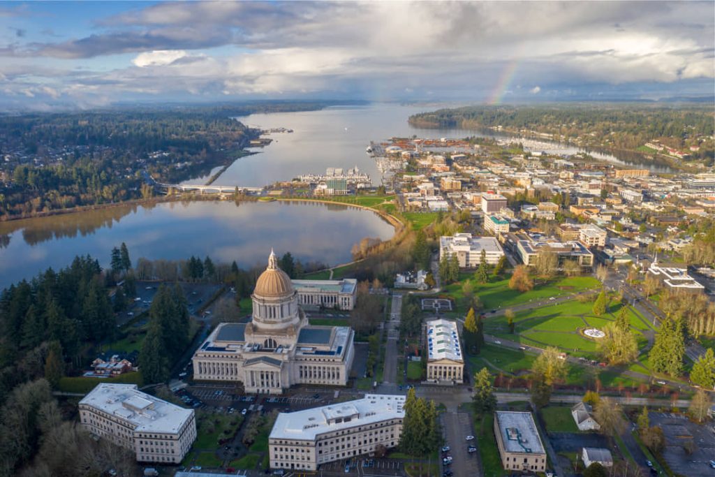 Luchtfoto van het koepelgebouw van het Washington State Capitol met de stad Olympia, een meer en een regenboog op de achtergrond