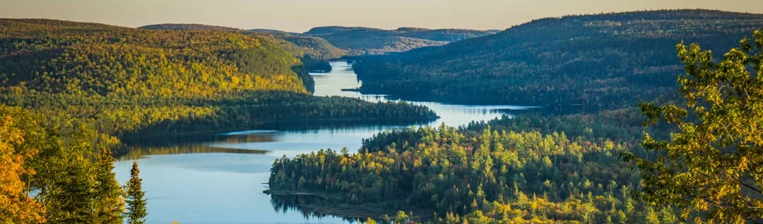 Panoramisch uitzicht vanaf een heuvel over een kronkelend meer omgeven door glooiende, bosrijke heuvels in Oost-Canada