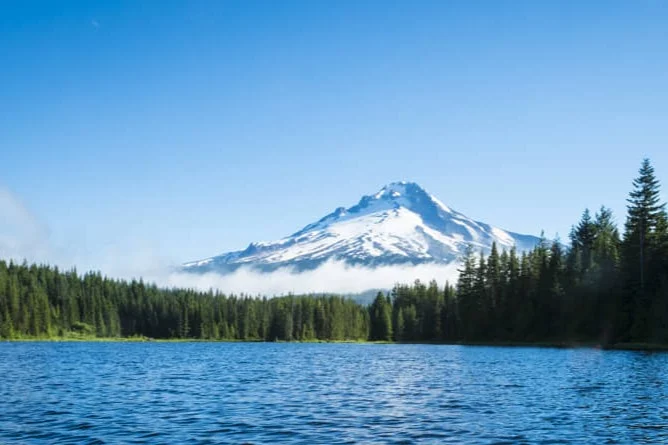 Een besneeuwde vulkaantop steekt boven de mistige boomtoppen uit bij een helderblauw meer in de Pacific Northwest