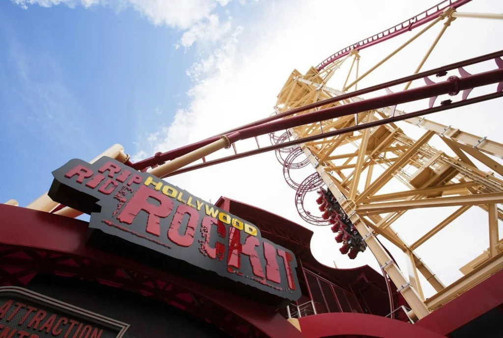Rood en geel bord met de tekst Hollywood Rip Ride Rockit onder de rails van een achtbaan