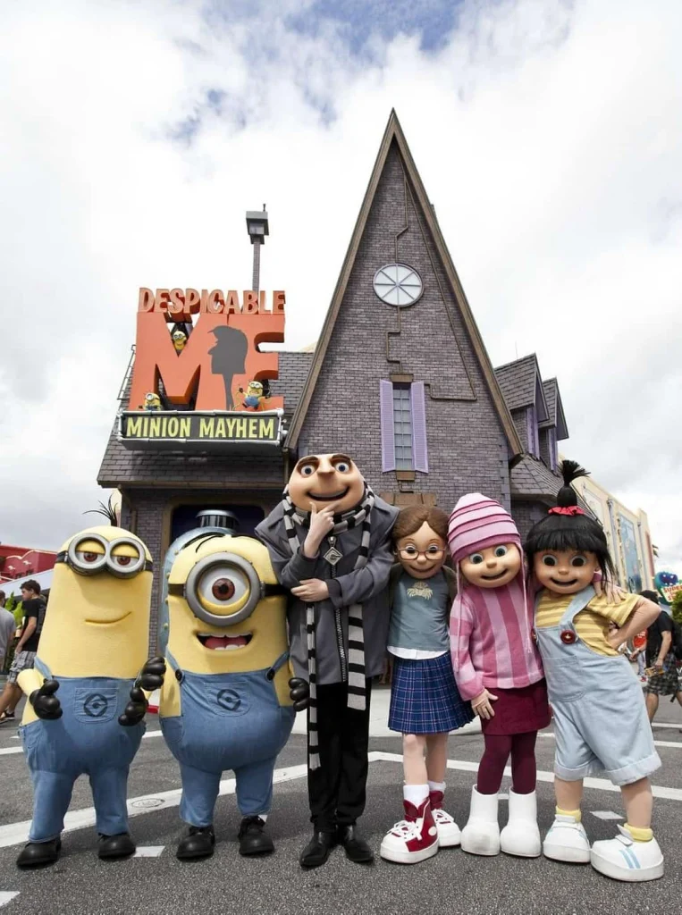 Gezin poseert met de personages Gru en twee Minions voor het gebouw van de attractie Despicable Me Minion Mayhem