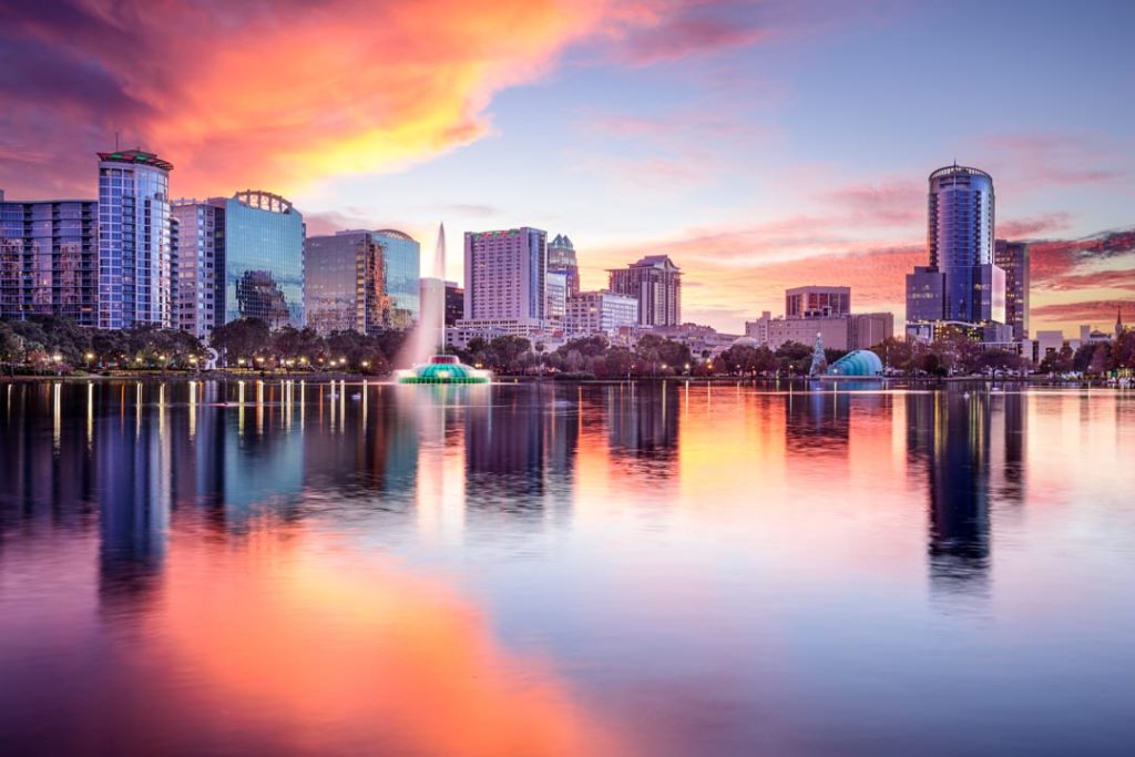 De verlichte fontein van Lake Eola Park met de skyline van Orlando erachter, weerspiegeld in het water bij een kleurrijke zonsondergang