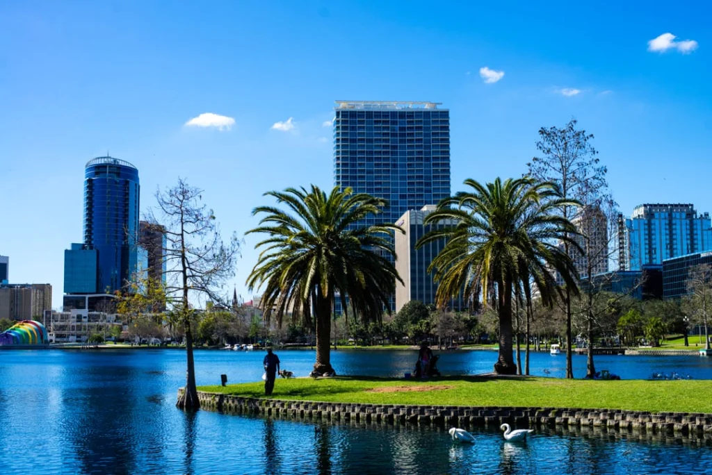 Blauw meer in Lake Eola Park in Orlando met palmbomen, wandelaars en zwanen op het water tegen de hoge gebouwen van de skyline