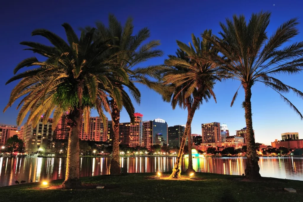 Palmbomen omlijsten de verlichte skyline van Orlando die weerspiegelt in het water van Lake Eola bij avondschemering