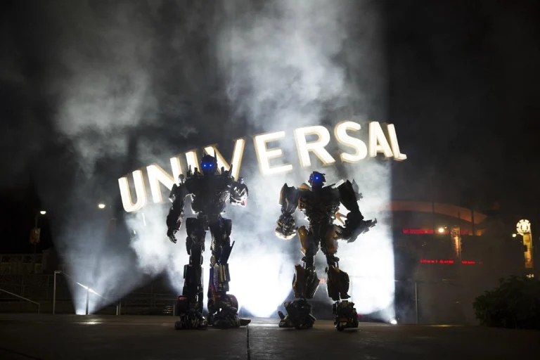 Twee levensgrote Transformers robots staan in rook voor het verlichte Universal logo tijdens een avondshow in Orlando