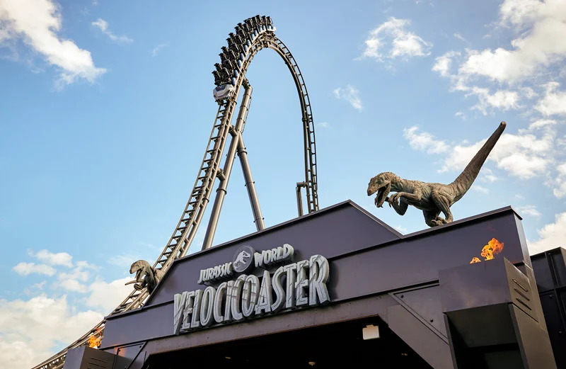 Bezoekers razen over de Velocicoaster achtbaan langs een levensgroot dinosaurusstandbeeld in Universal Orlando