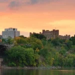 IJzeren spoorbrug over de rivier met op de achtergrond het kasteelachtige Château Laurier onder een oranje avondlucht in Ottawa