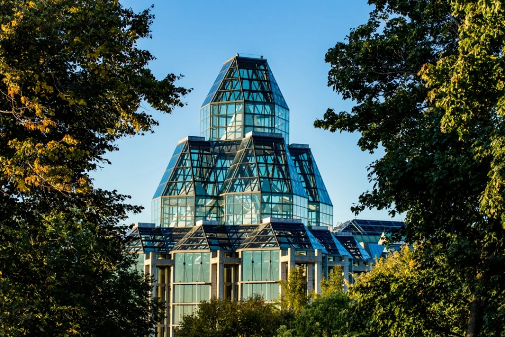 Piramidevormige glazen koepel van een museumgebouw die boven de bomen uitsteekt tegen een blauwe hemel in Ottawa