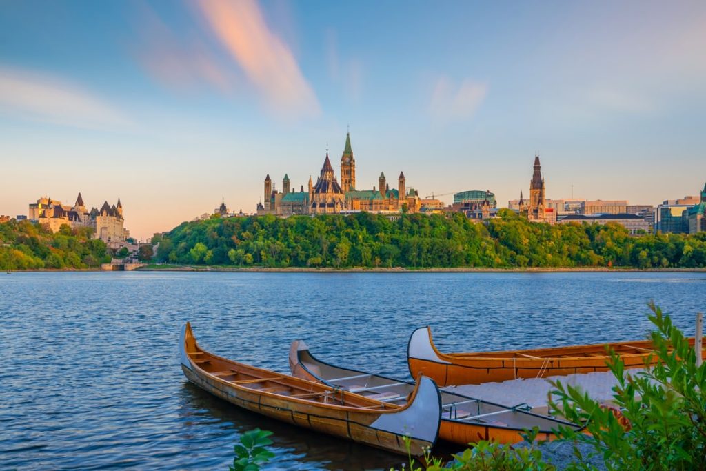 Houten kano's met een opvallend gebogen boeg liggen afgemeerd op de rivier terwijl Parliament Hill in de avondzon oplicht