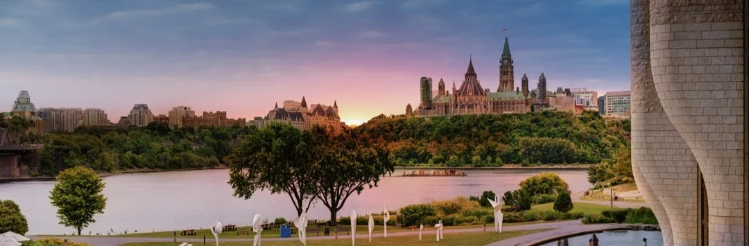 Uitzicht vanaf een terras op de parlementsgebouwen van Ottawa aan de rivier bij zonsondergang, met een roze en gouden lucht