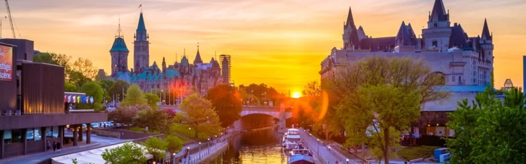 Torens van de Canadese parlementsgebouwen boven een kanaal met boten, verlicht door een gouden zonsondergang