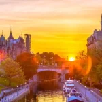 Torens van de Canadese parlementsgebouwen boven een kanaal met boten, verlicht door een gouden zonsondergang