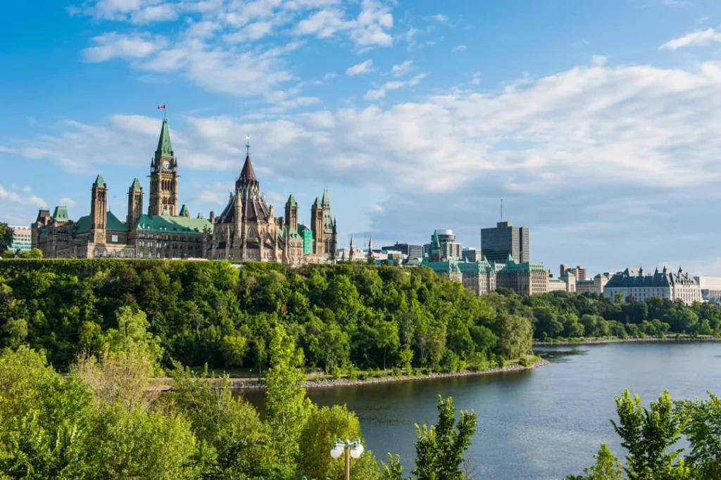 Het parlementsgebouw van Ottawa op een groene heuvel boven de rivier, gefotografeerd op een heldere zomerdag