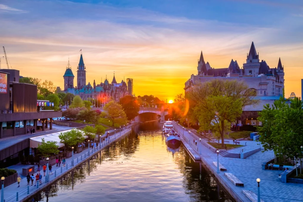 Boot op het Rideaukanaal in Ottawa bij een gouden zonsondergang, met het Château Laurier en het parlementsgebouw op de achtergrond