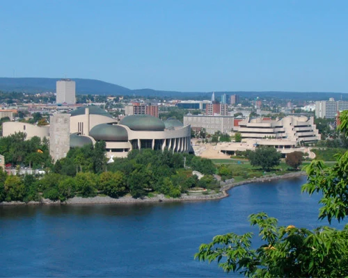 Panorama vanaf een heuvel over de rivier naar een modern museumgebouw met golvende koepeldaken en de skyline van Gatineau op de achtergrond