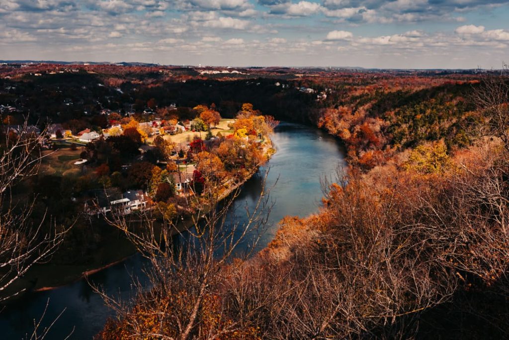 Kronkelende rivier omgeven door bos in oranje en gele herfstkleuren, met huizen op een landtong langs de oever in de Ozarks