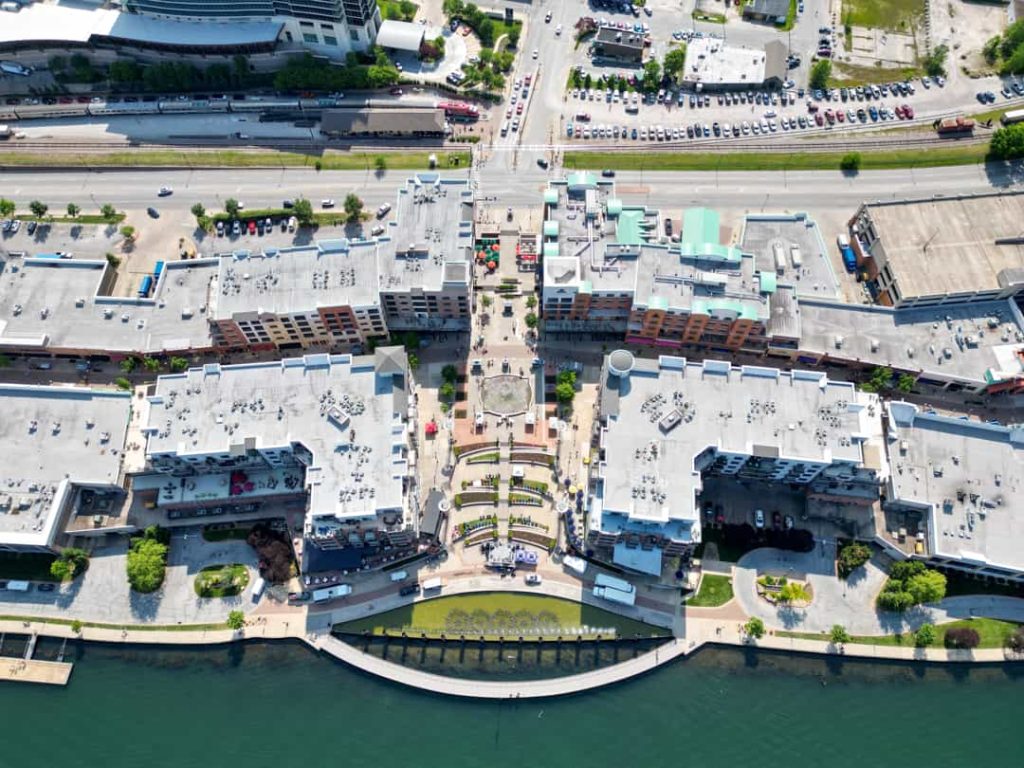 Luchtfoto van een groot resort met platte daken, terrassen en een plein rond een fontein, gelegen aan het water van een meer