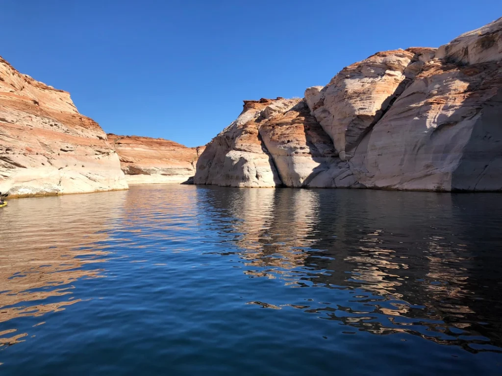 Lichte zandstenen rotswanden weerspiegeld in het kalme donkerblauwe water van een baai van Lake Powell bij Page