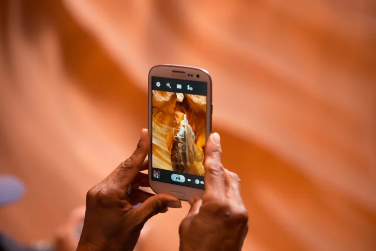 Close-up van twee handen die met een smartphone een foto maken van de golvende oranje wanden van Antelope Canyon