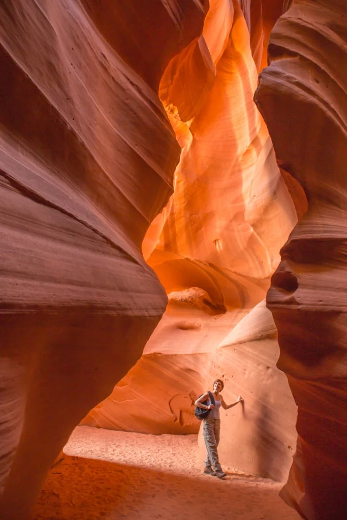 Wandelaar met rugzak en wandelstok staat tussen de hoge oranje gloeiende zandstenen wanden van Antelope Canyon